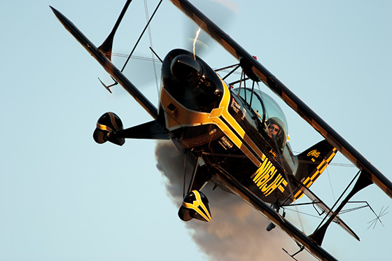 The frame the campaign was built from: Jon Melby's black and yellow Pitts biplane banking against a plain blue sky, trailing smoke — the photograph the storm sky was composited into.